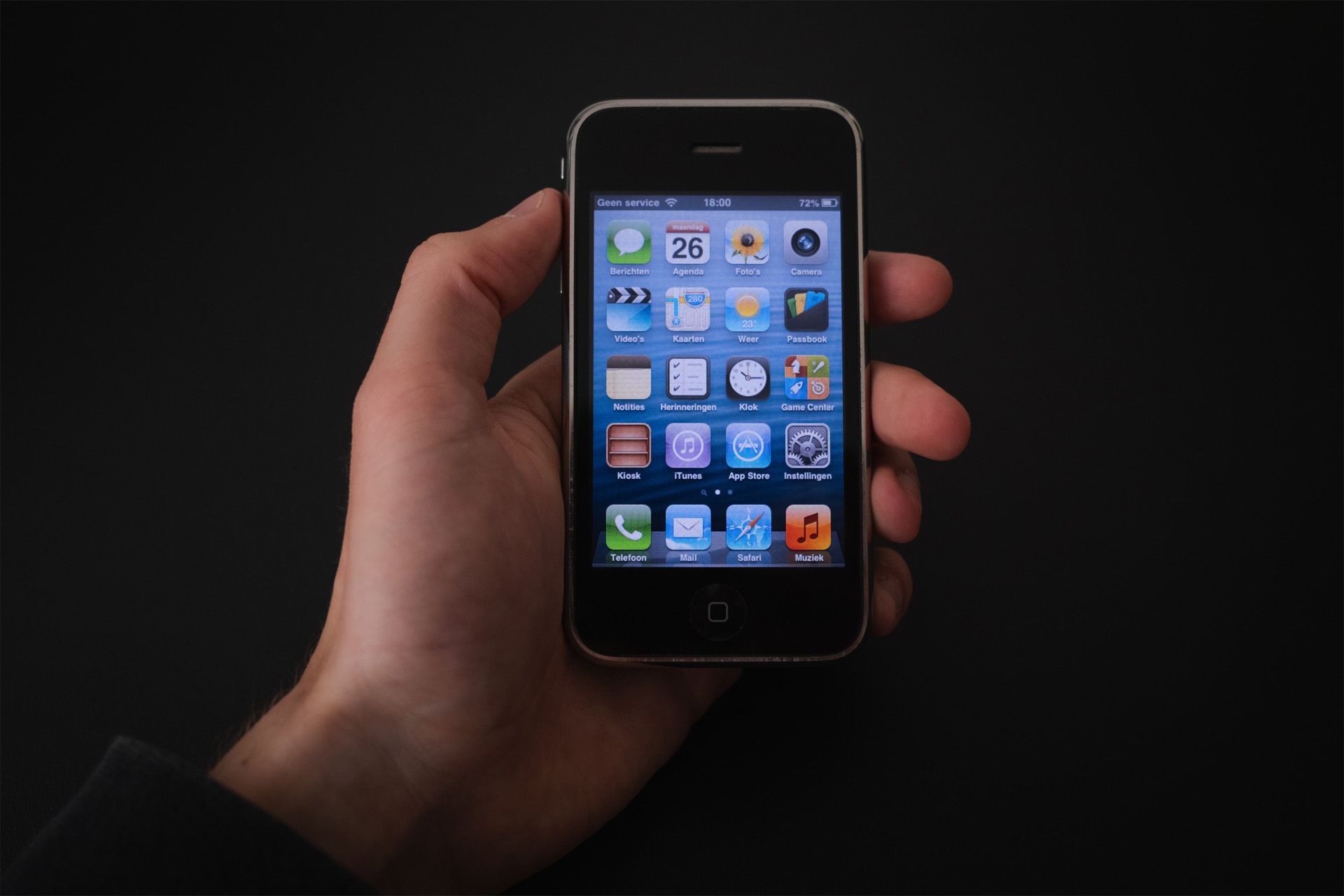 A person holding an iPhone 3GS with iOS 6 running on it.